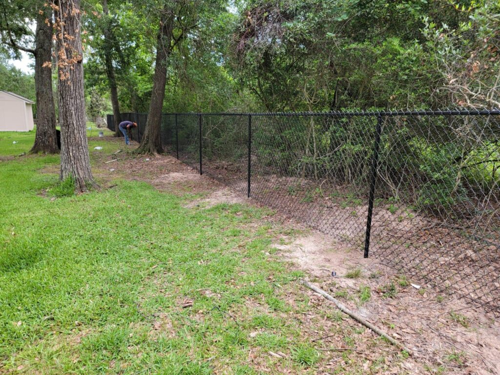 houston chain link fence trees yard - Mustang Fencing and Gates "Chain-link fence surrounding a lush yard with mature trees in Houston, perfect for fencing and gates services."