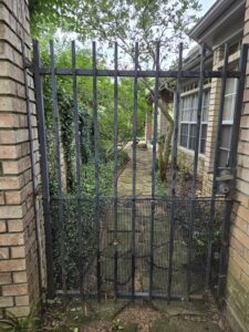 "A metal gate and brick fence in a yard in Houston, Texas, provided by Mustang Fencing and Gates."