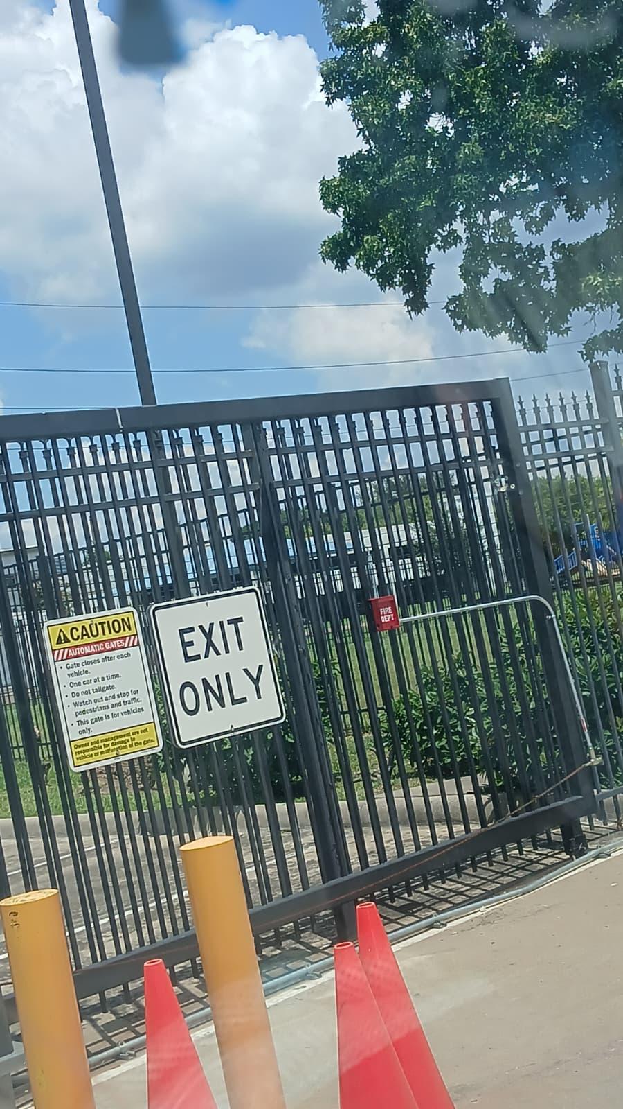 Black steel automatic vehicle gate with Exit Only signage and safety bollards at a commercial property