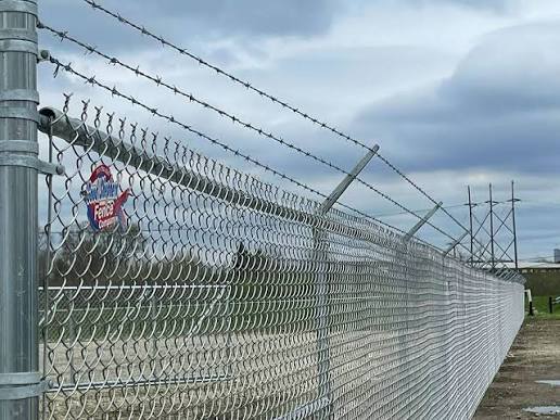Galvanized chain-link fence topped with barbed wire near power-line towers at an industrial property in Houston