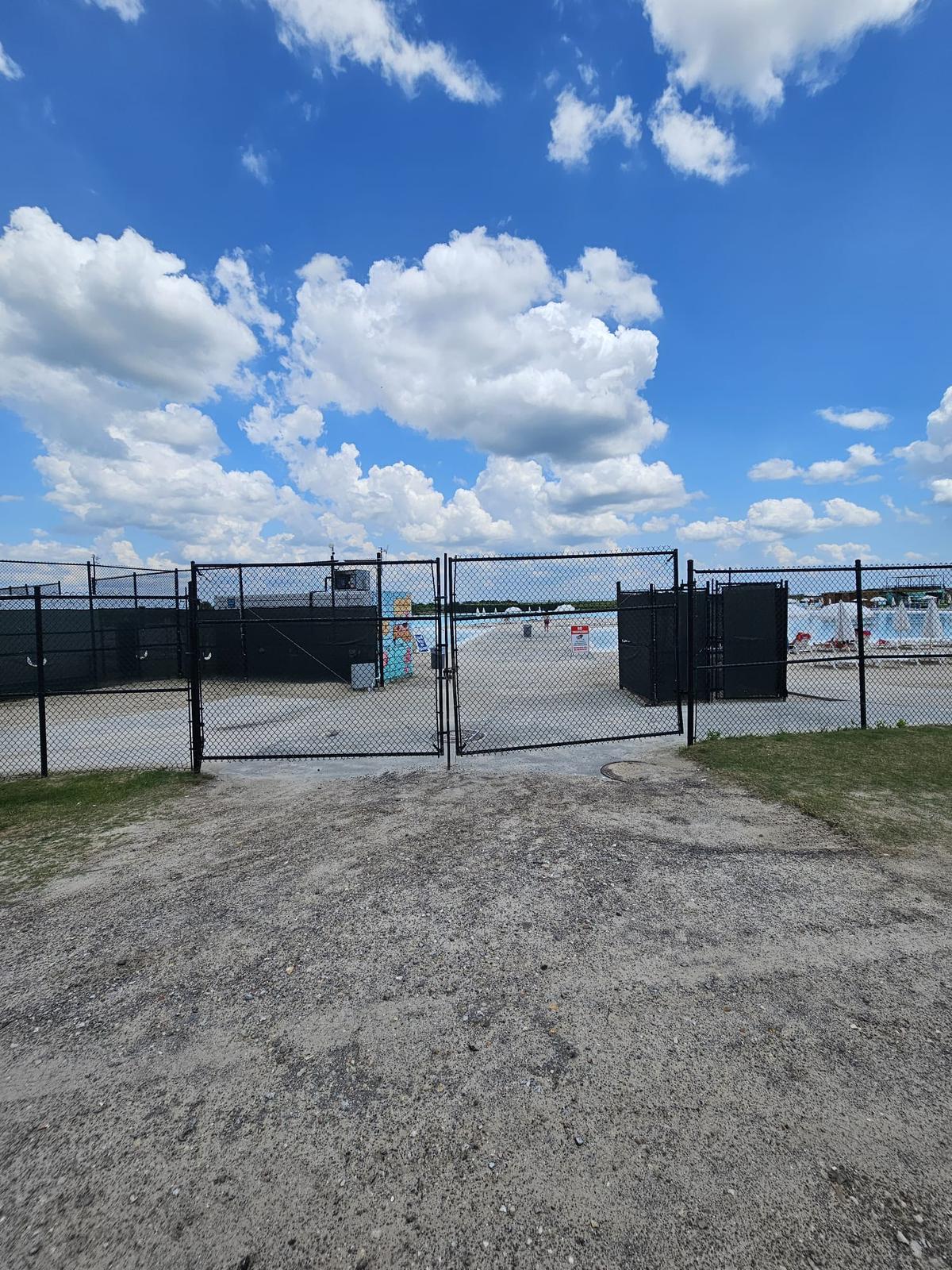 Black chain-link perimeter fence with a double swing gate enclosing a commercial community amenity area near Houston