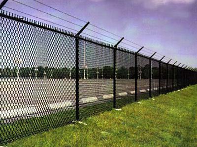 Chain-link security perimeter fence topped with three-strand barbed wire around an industrial lot near Houston