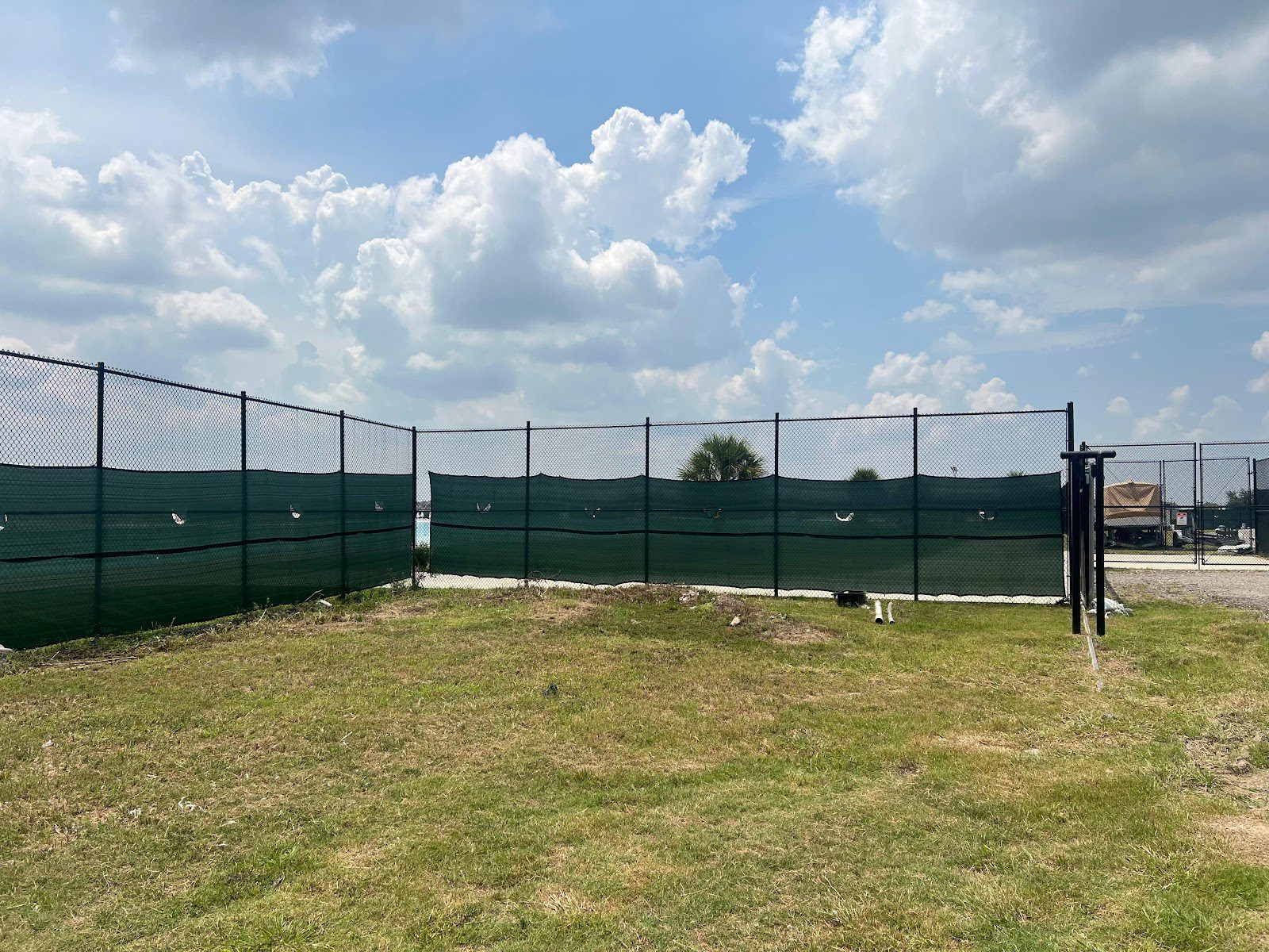 Corner run of black chain-link fence with green privacy windscreen on a Houston-area commercial lot