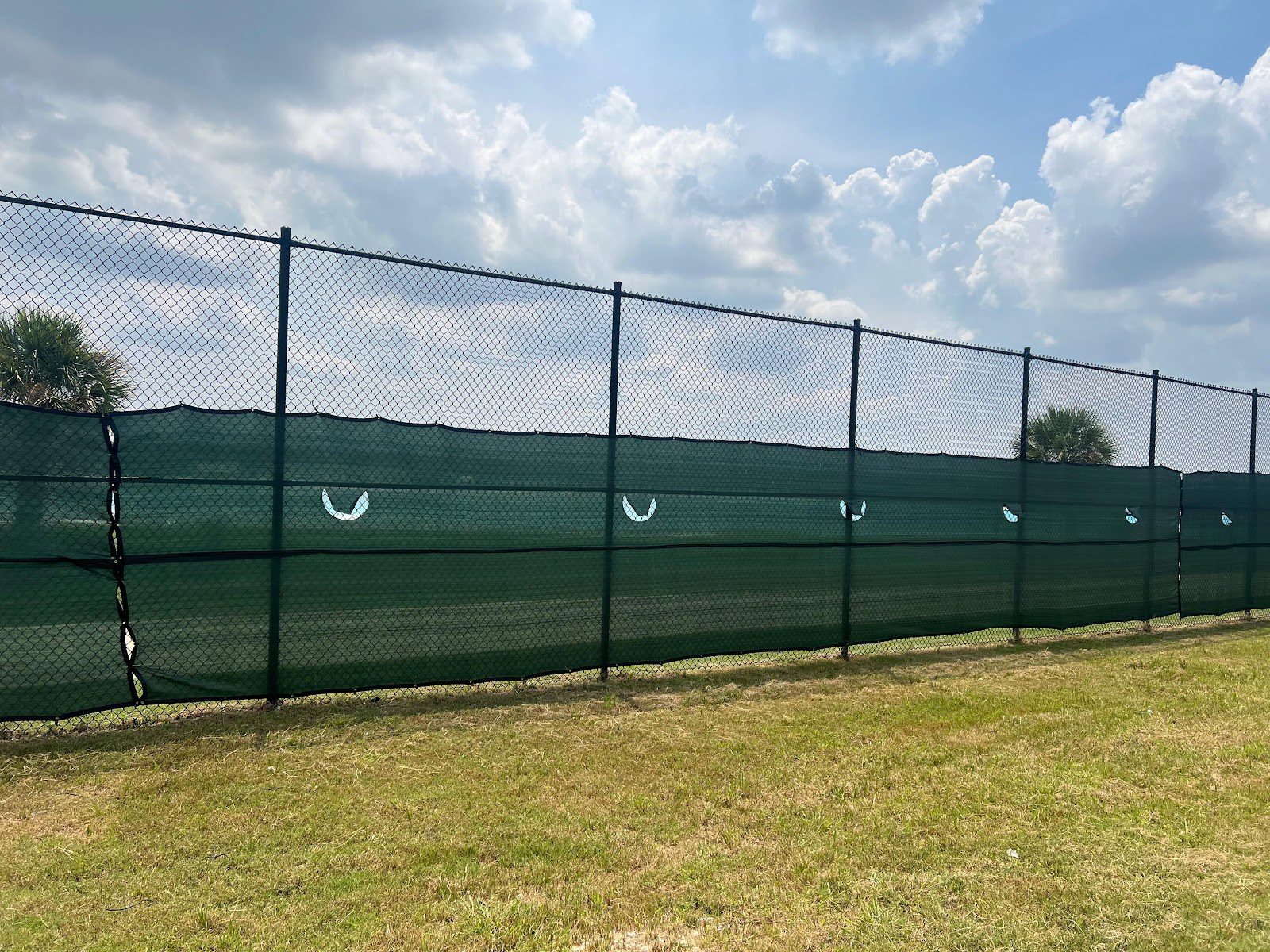 Long straight run of black chain-link fence with a green privacy windscreen along a commercial perimeter