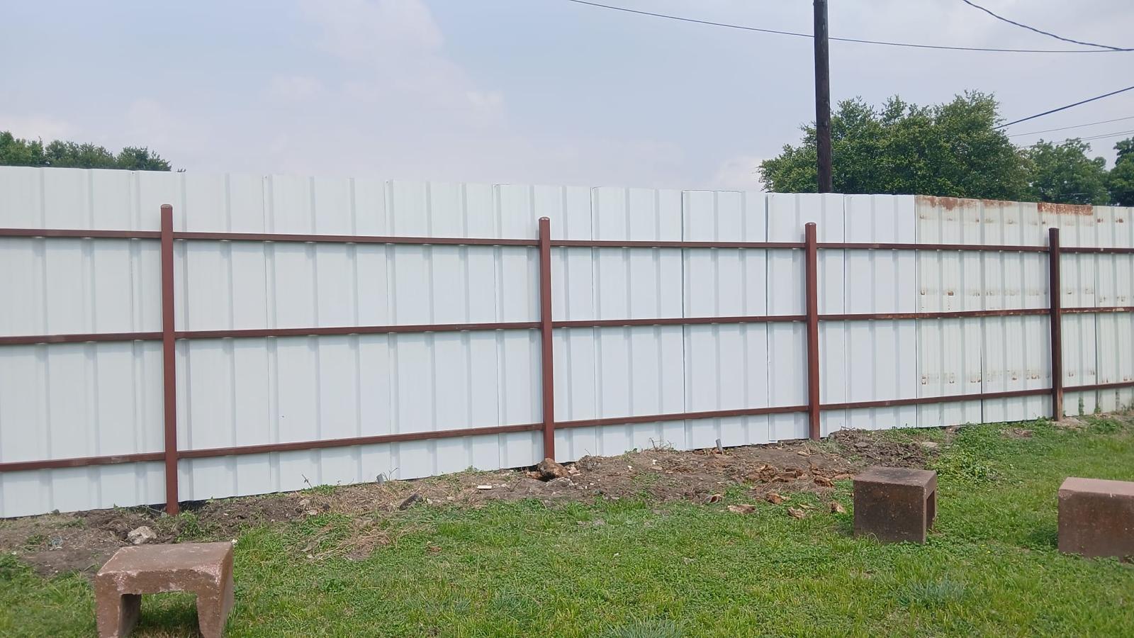 Privacy fence built from corrugated-metal panels on steel rails and posts along a property line