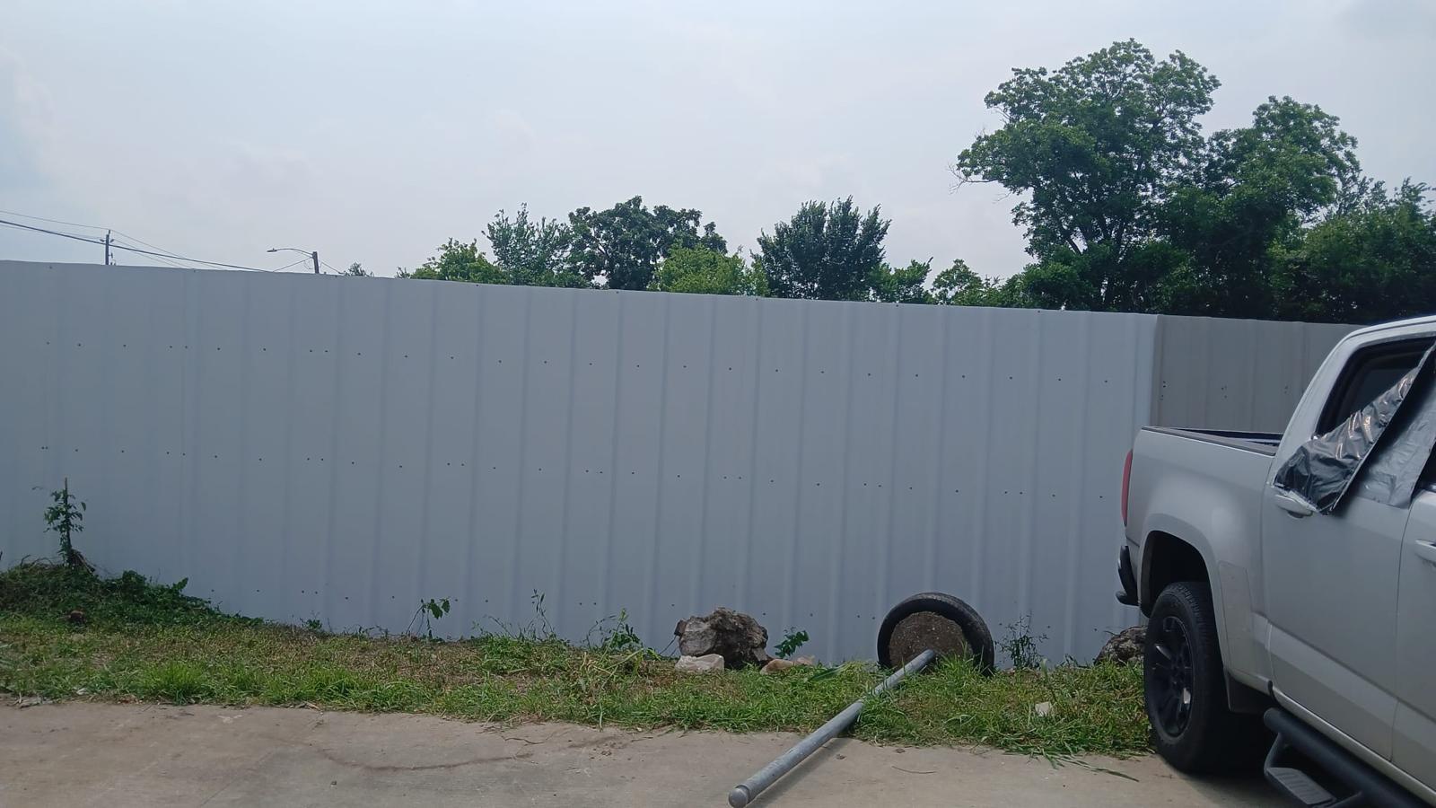 Tall grey corrugated-metal perimeter privacy fence enclosing a commercial lot in the Houston area