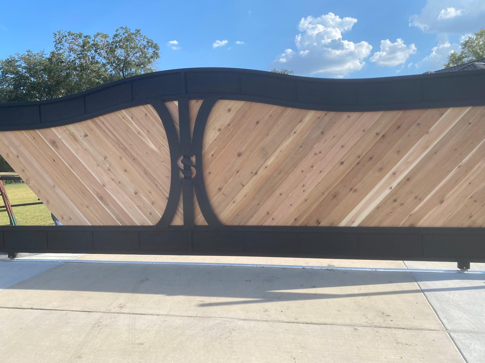 Close-up of a custom steel-frame sliding gate with a decorative scrolled monogram medallion and cedar panels