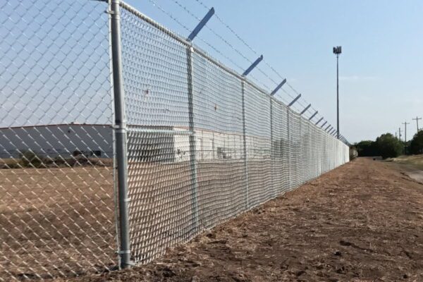 Galvanized chain-link security fence topped with angled barbed wire protecting an industrial facility near Houston