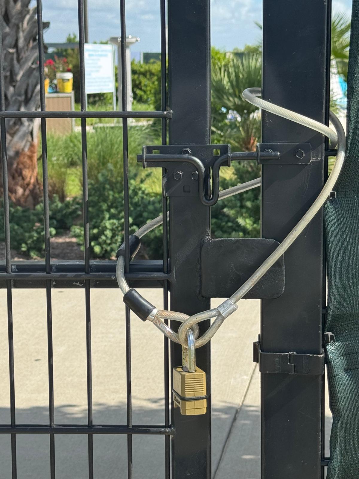 Close-up of a black metal gate secured with a slide-bolt latch and padlock at a Houston-area community amenity