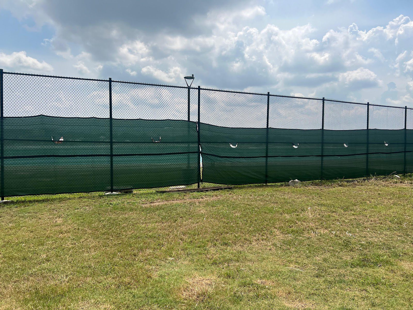 Green vinyl-coated chain-link fence with a privacy windscreen around a grassy commercial field