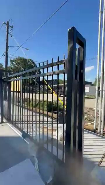 A tall black steel picket cantilever slide gate rolls open across a poured-concrete commercial lot, delivering smooth motorized entry for high-traffic business sites.