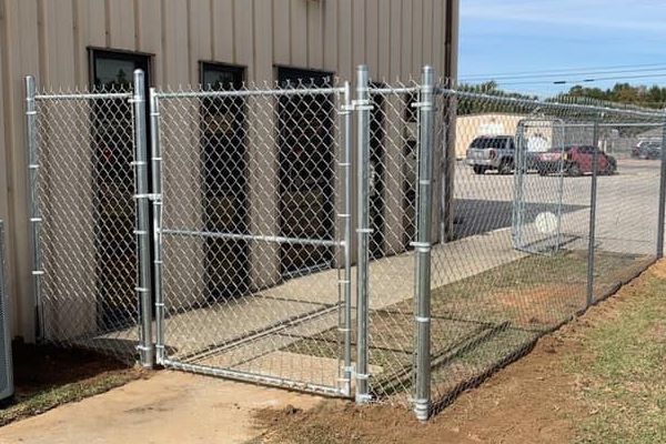 A tight look at a galvanized chain-link panel enclosure anchored securely at ground level against a commercial building.