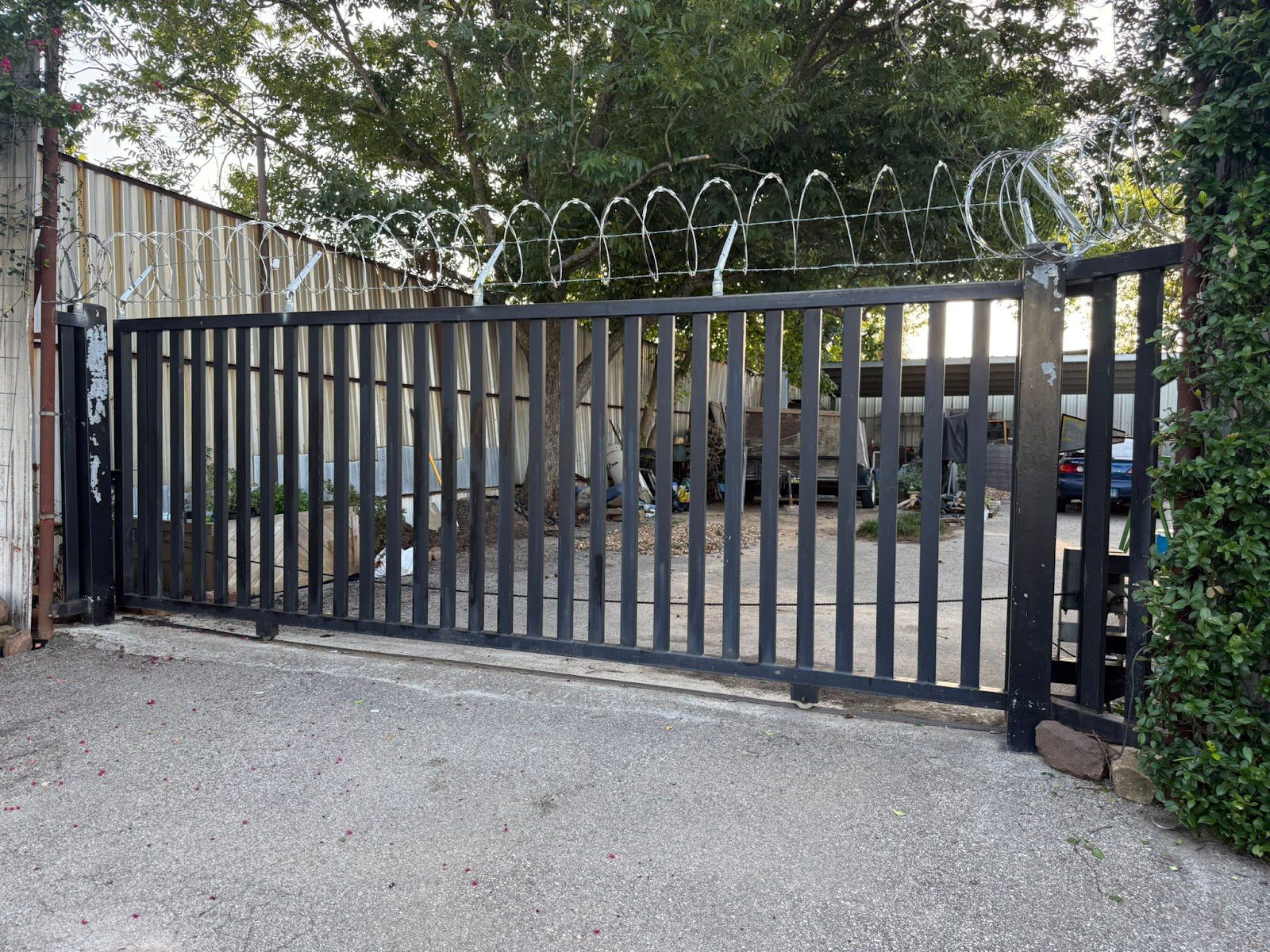 A steel picket slide gate topped with a coil of concertina razor wire hardens the vehicle entrance to an industrial storage yard.