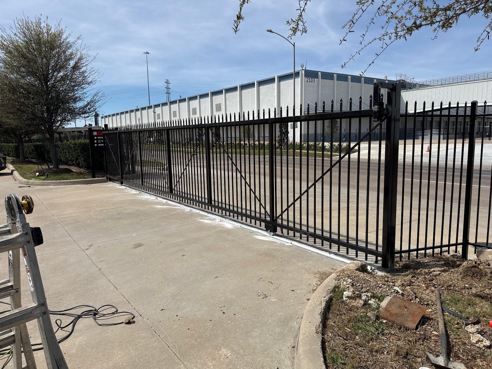 A freshly installed black steel spear-top cantilever slide gate stands at the entrance of a commercial distribution facility, its electric operator mounted and ready to run.