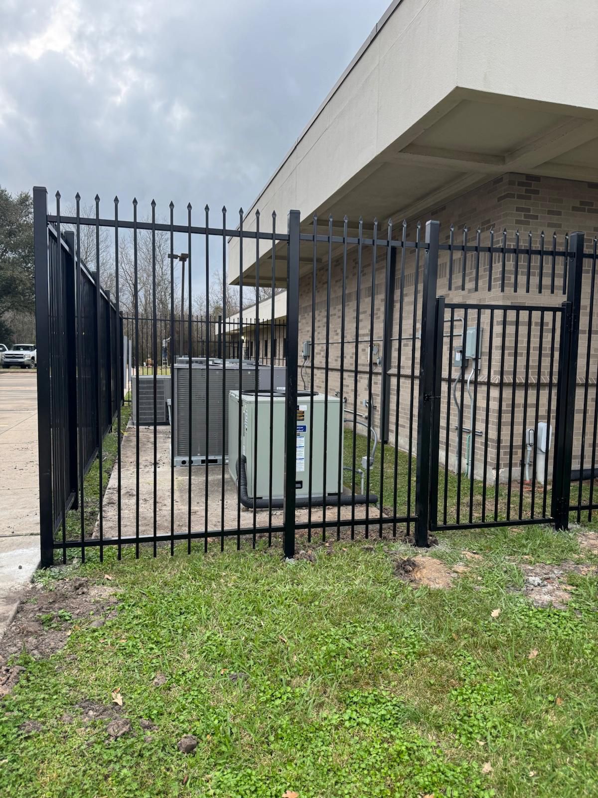An ornamental steel spear-top pedestrian swing gate set into a security enclosure at a brick professional building, blending clean curb appeal with controlled entry for a Bellaire courtyard.
