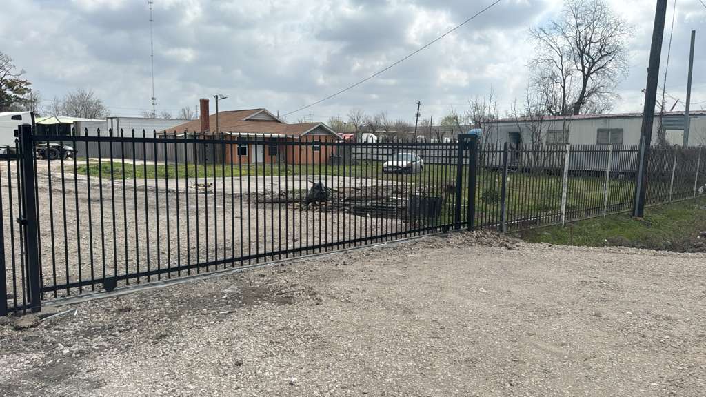 A black steel spear-top slide gate and its matching picket fence line secure a commercial yard, the leaf parked back along the perimeter to leave a clear drive-through opening.