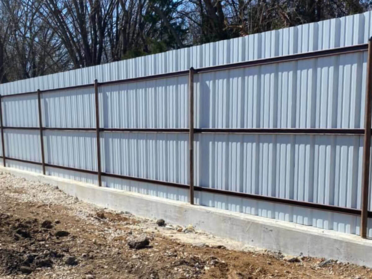 Heavy steel line posts set on a poured-concrete base anchor a corrugated-steel screen running the length of the property line.