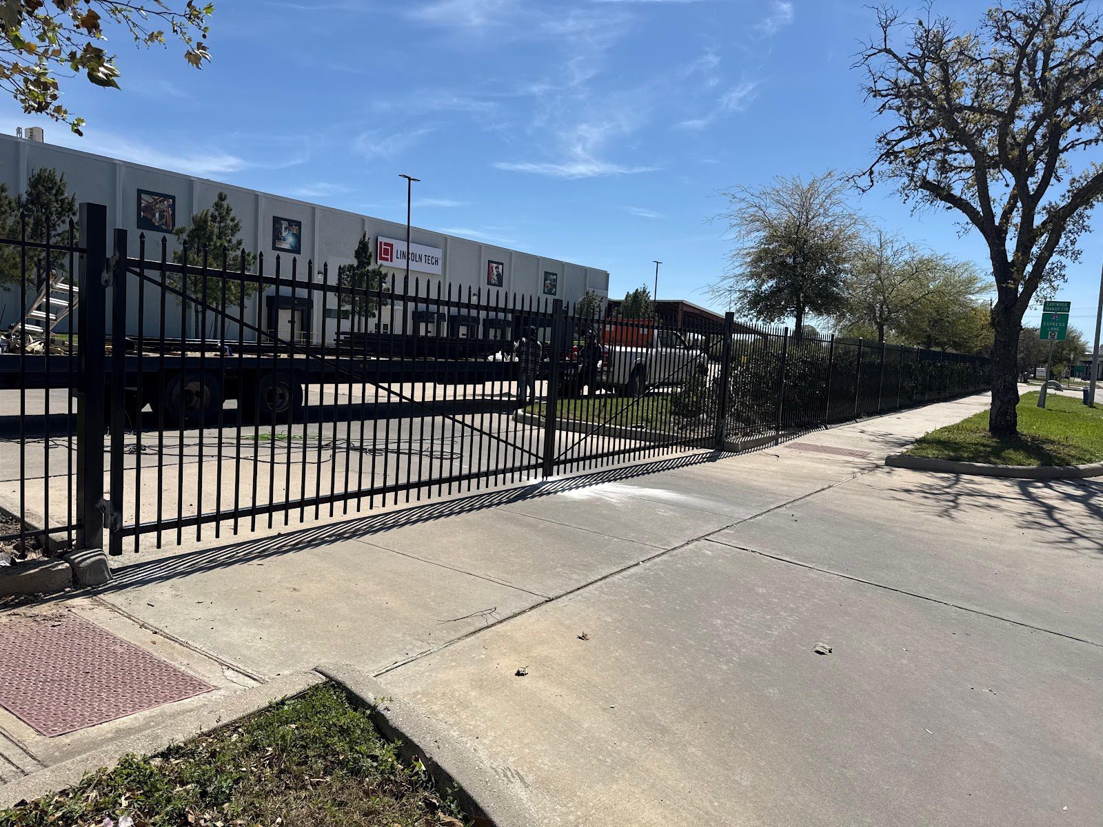 Black spear-top ornamental steel fencing and a matching cantilever slide gate line the sidewalk of a professional campus, a crisp, secure frontage that suits Bellaire's medical and office corridors.