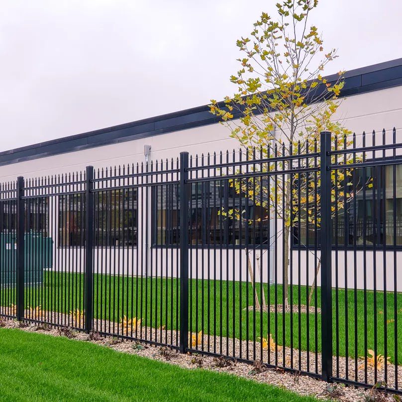 An ornamental steel picket fence with pressed-spear tops frames the landscaped lawn of a modern single-story commercial building, mirroring the polished street presence boutique storefronts want along Bellaire Boulevard.