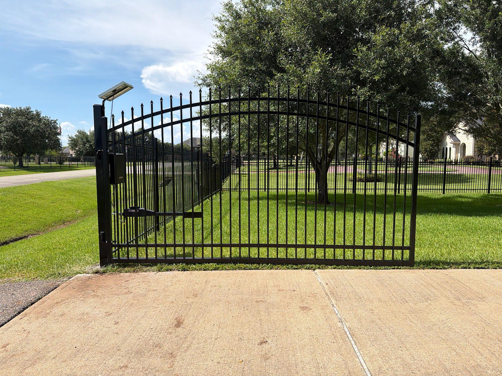 An arched-top ornamental swing gate with an automatic operator ties seamlessly into a matching perimeter fence line at an upscale community entrance.