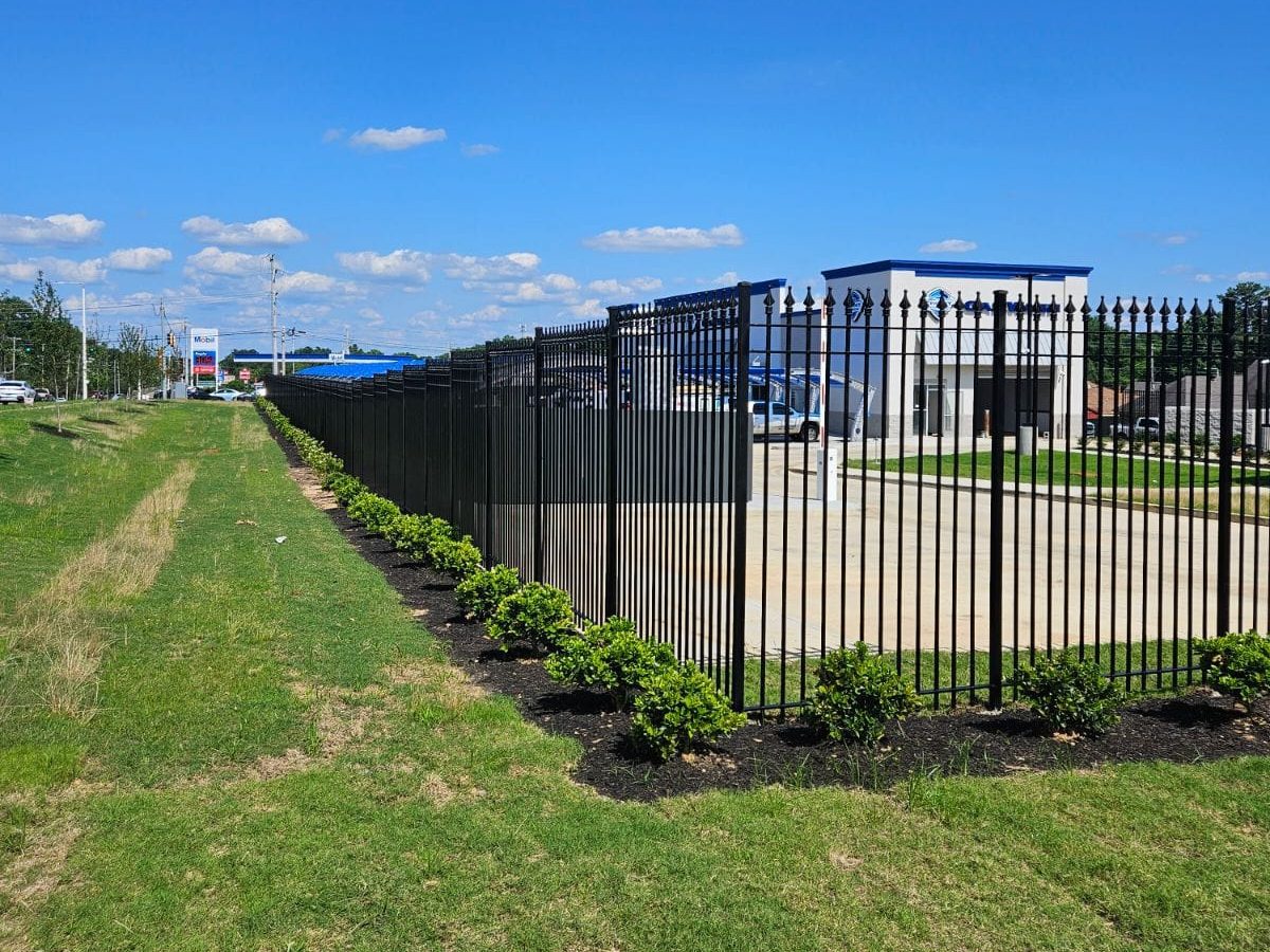 A tall black ornamental steel fence with spear-point finials wraps a landscaped commercial office frontage, the kind of established, secure perimeter Mustang Fencing and Gates builds for professional 