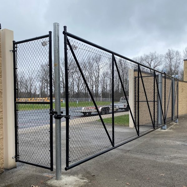 This black chain-link double swing gate, diagonally braced and hung between a stucco pillar and a masonry building, secures the entrance to a paved commercial lot, providing practical gated access for Bellaire-area parking areas.