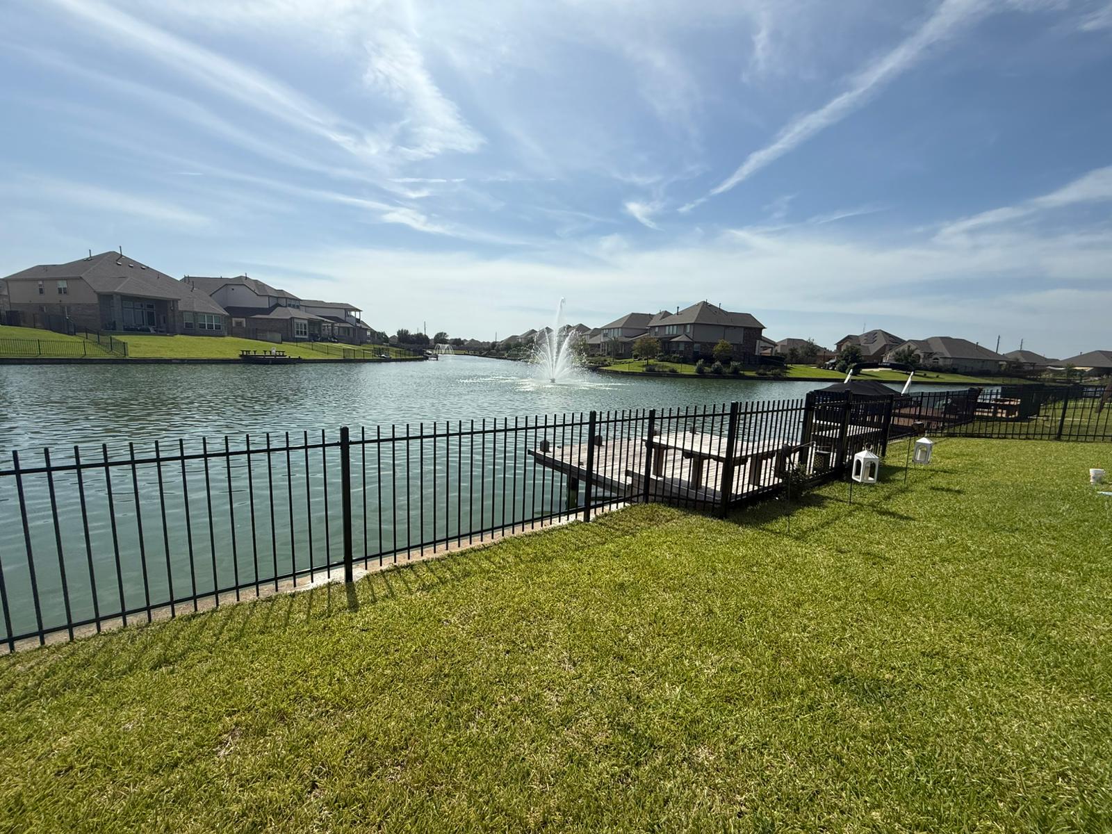 A black spear-top perimeter fence runs cleanly along a manicured community lakefront, holding a uniform line and height.