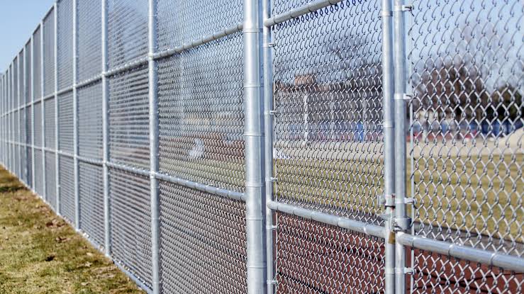A low shot down a galvanized chain-link line shows the fabric pulled drum-tight along the bottom rail to grade.