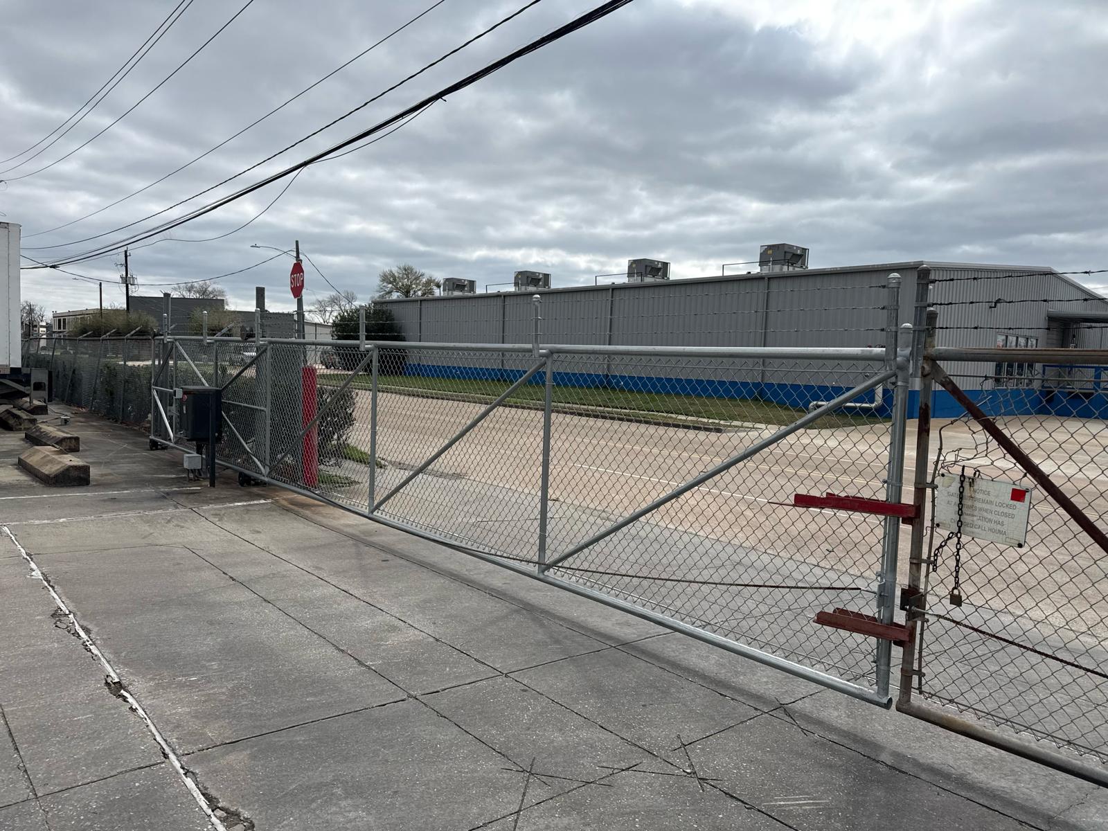 A galvanized chain-link cantilever slide gate with barbed-wire top and electric operator secures the entrance to an industrial warehouse and distribution property.