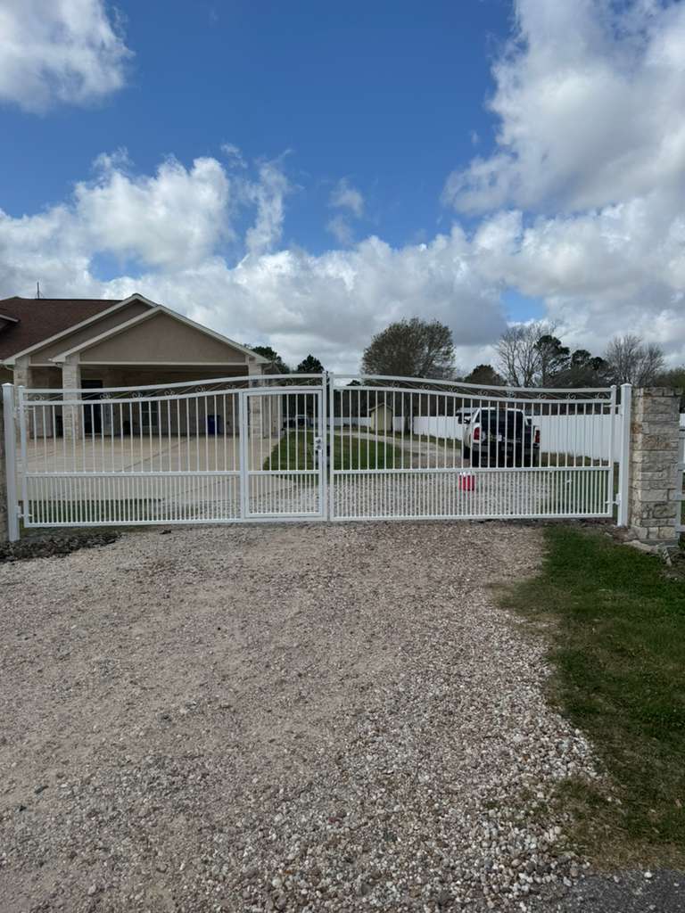 A white powder-coated ornamental double swing gate framed by stone columns creates a stately gated community entrance.