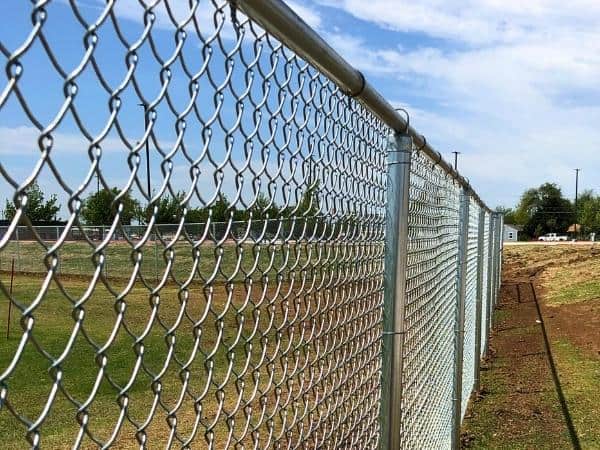 A clean galvanized chain-link perimeter with round steel line posts and top rail running the length of an open site.