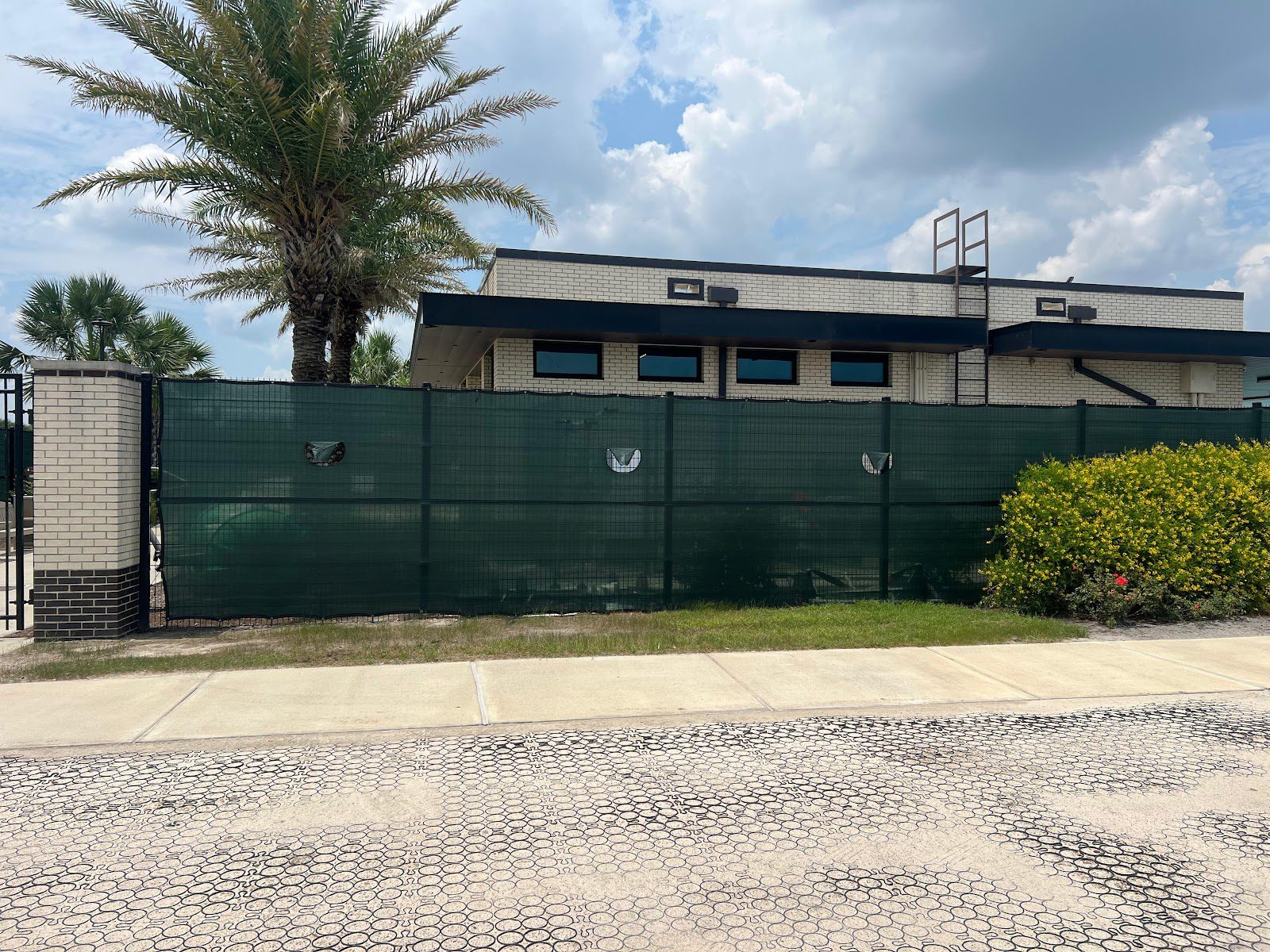 Black chain-link fencing fitted with solid green privacy screening running along the frontage of a commercial building.
