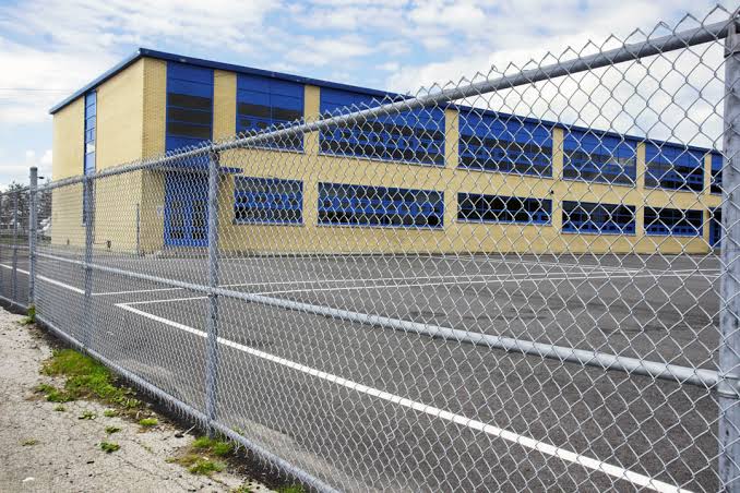 A galvanized chain-link perimeter securing the paved lot in front of a nearly complete commercial building.