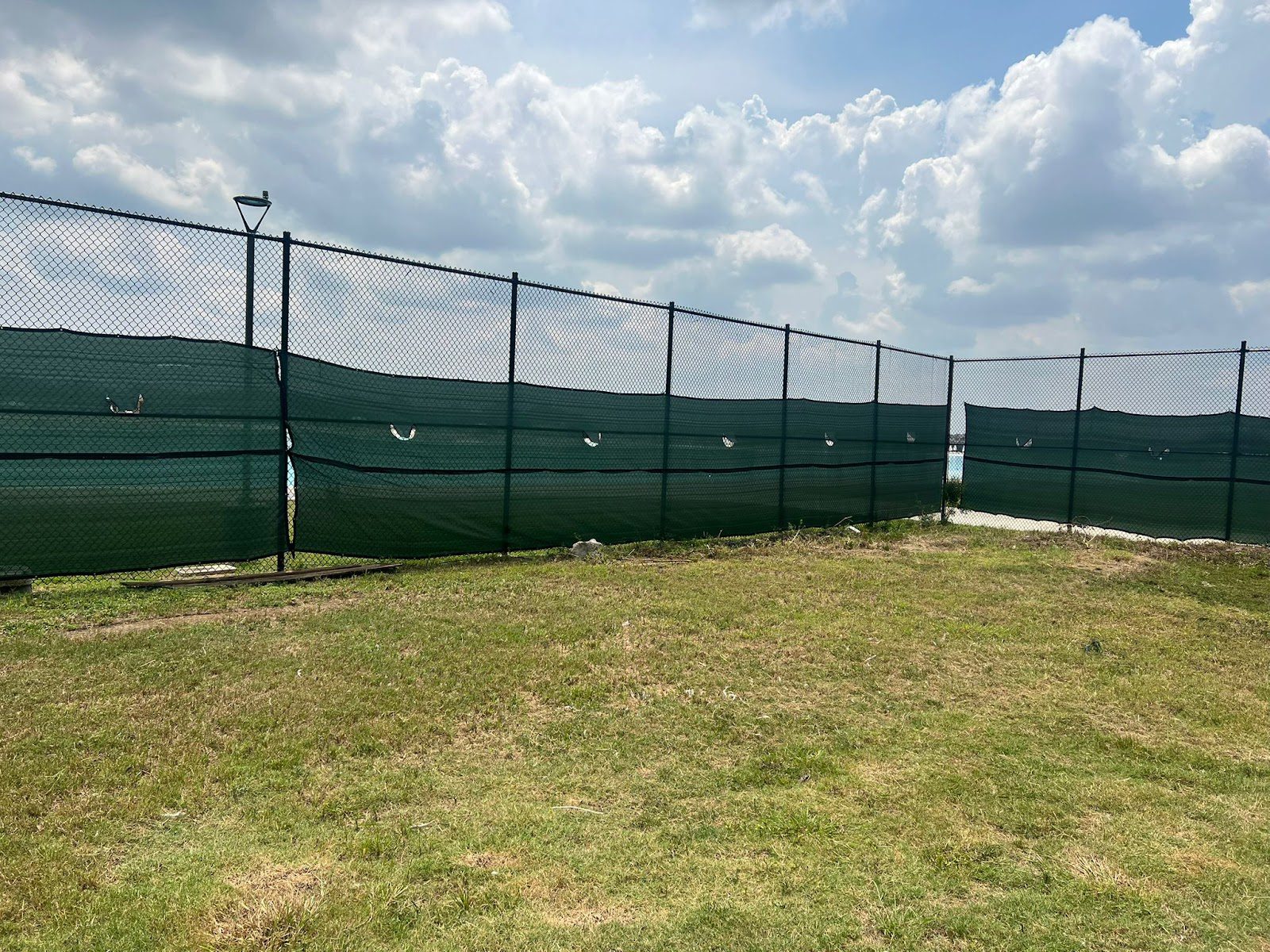 A continuous chain-link perimeter run fitted with a partial green privacy wind screen enclosing the property edge.