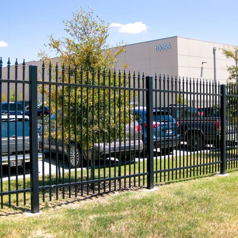 Black spear-top ornamental steel pickets run the length of a commercial property frontage, securing the parking lot without blocking sightlines to the storefront behind.