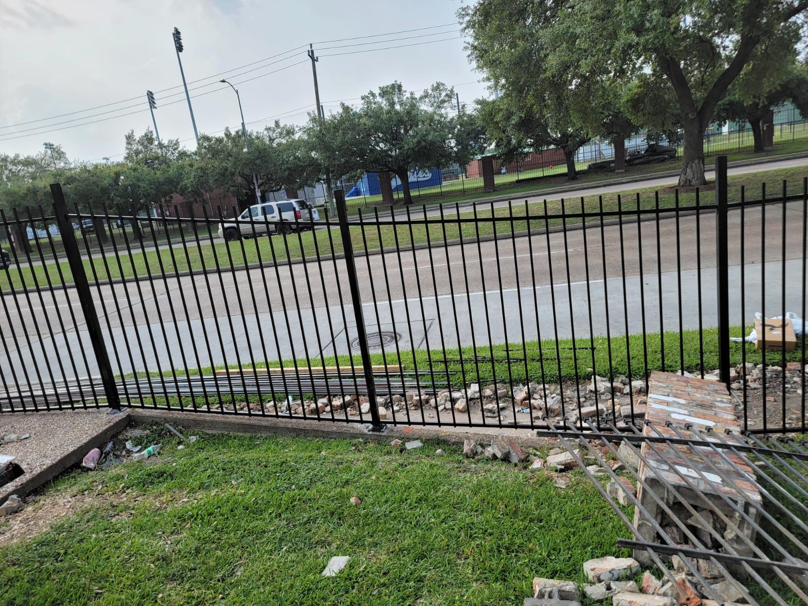 Black ornamental steel flat-top picket fence being installed along a roadway fronting a Houston-area sports complex