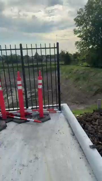 Newly installed black steel two-rail vertical-picket fence panel at an industrial site near Houston, with traffic barricade posts in front